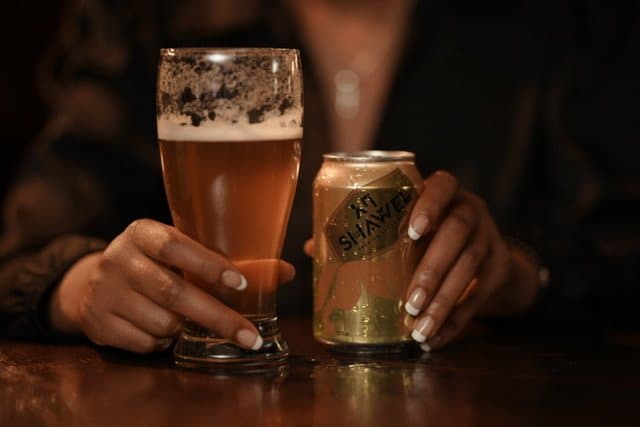 Hands around a Shawel can and a tall glass of beer at the bar