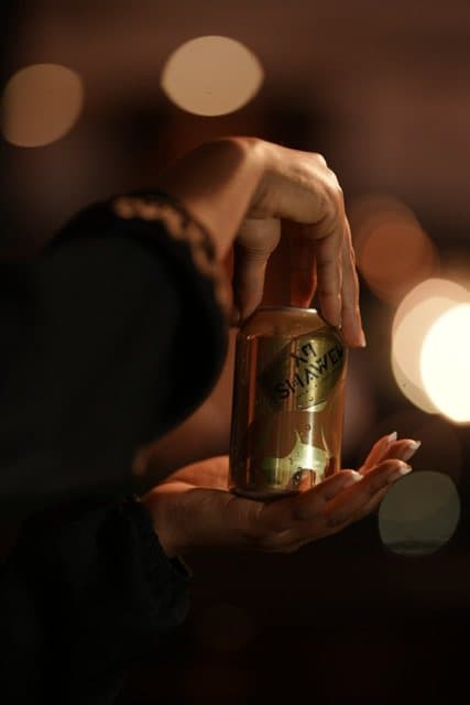 A hand holding a gold Shawel can against warm bokeh lights