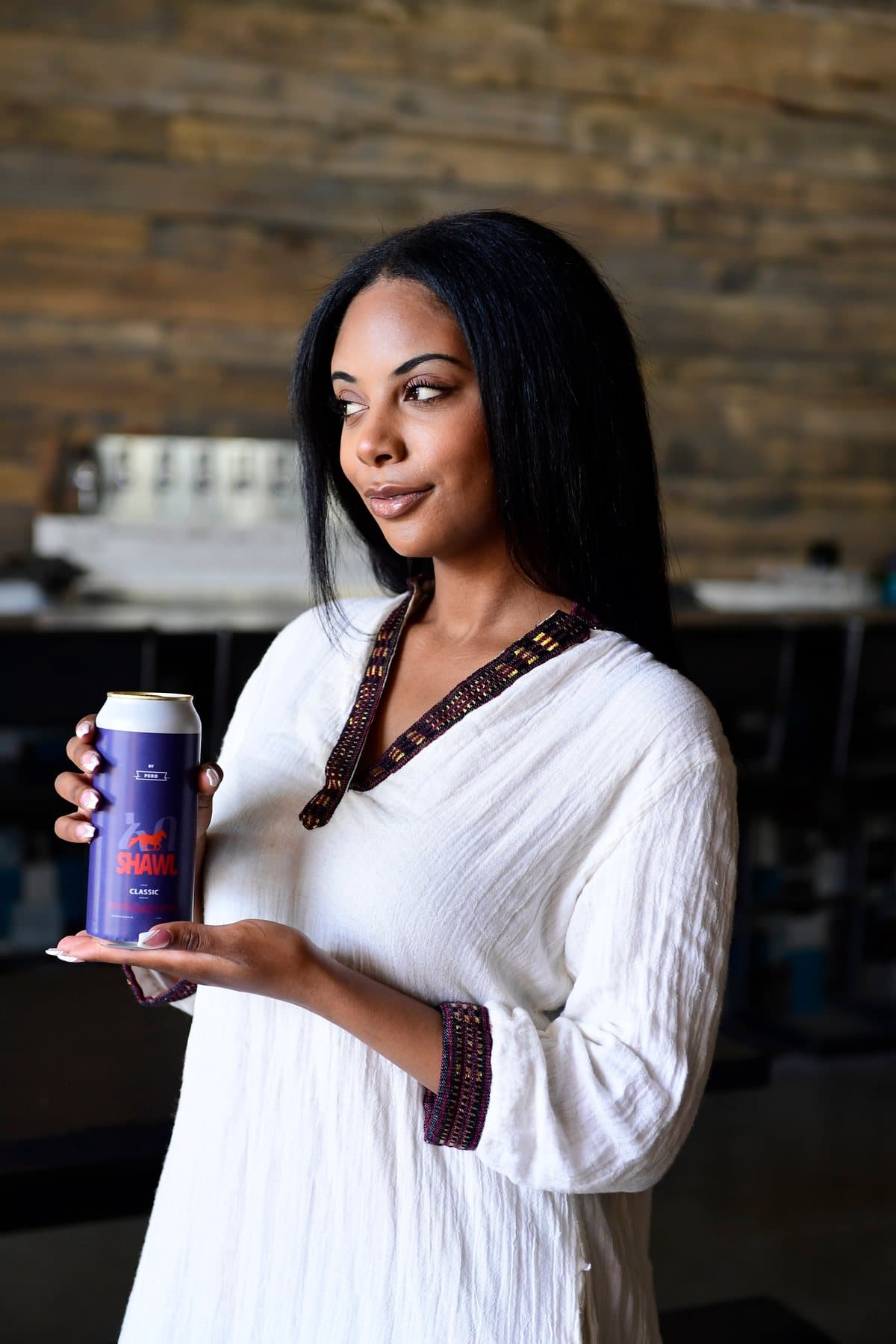 A woman in traditional white dress holding a Shawel Classic can