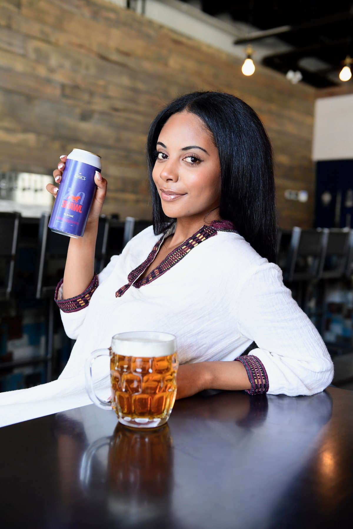 A woman in traditional white dress raising a full mug of Shawel with a can in hand