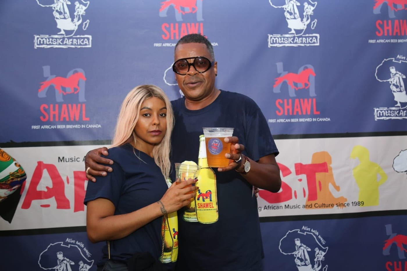 Two guests at AfroFest holding a Shawel beer and merch