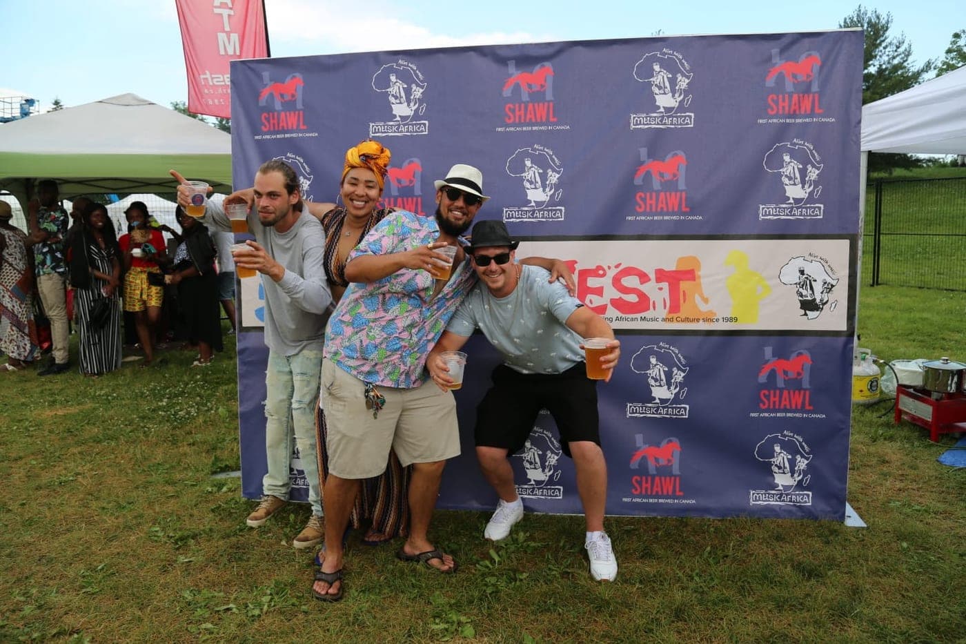 Friends striking poses with Shawel cups in front of the festival wall